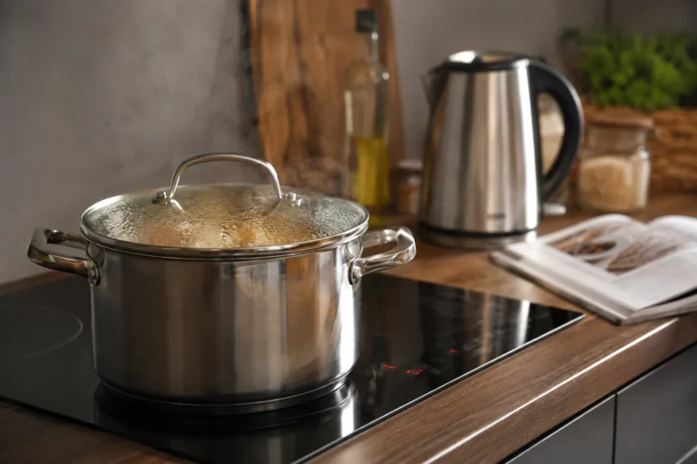 Garnek z pokrywką na płycie indukcyjnej i czajnik elektryczny w kuchni podczas oszczędnego gotowania