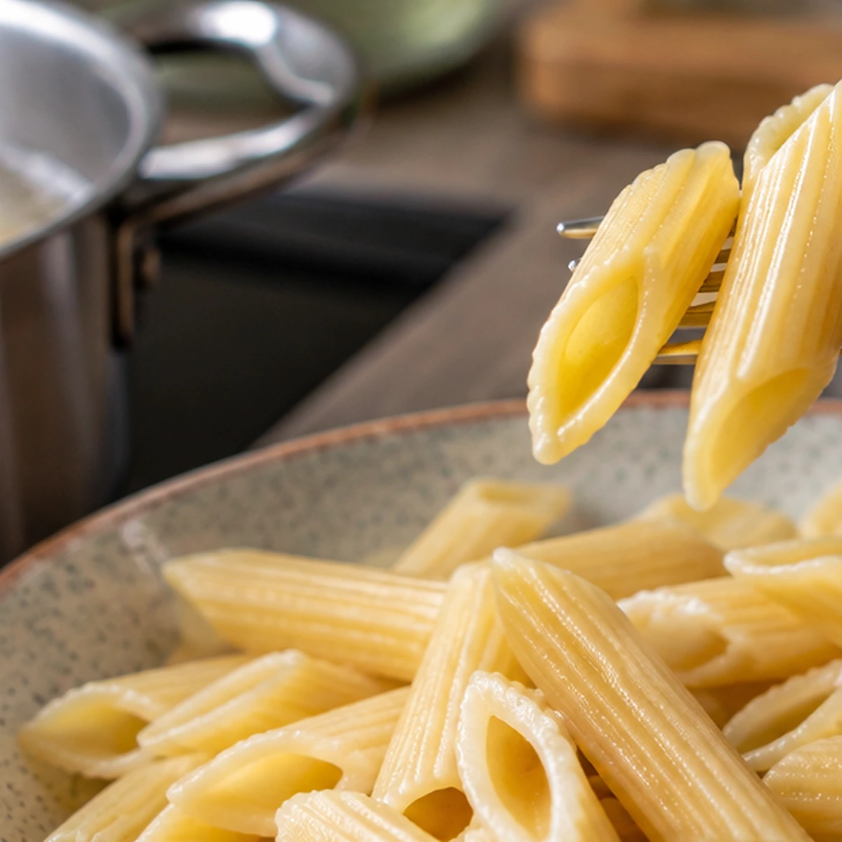 Ugotowany makaron penne na widelcu nad talerzem obok garnka z gorącą wodą